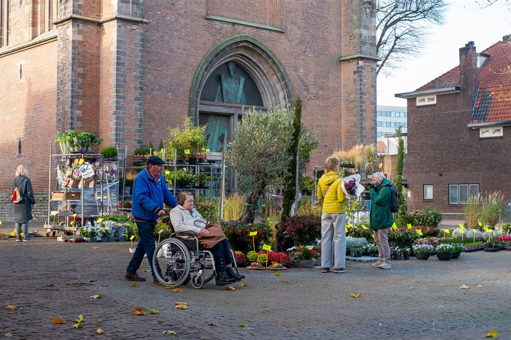  Een man duwt een vrouw in een rolstoel langs een bloemenkraam op het lieve vrouweplein 